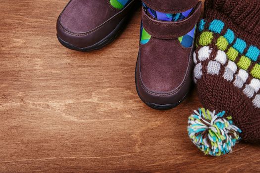 Winter children's boots and hat on the wooden textured background with copy-space for your text