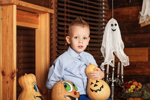 Halloween party with child holding painted pumpkin. Cute Little Boy having fun in Halloween decorations