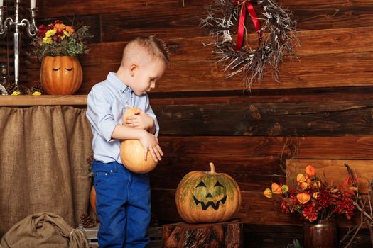 Halloween party with child holding painted pumpkin. Cute Little Boy having fun in Halloween decorations