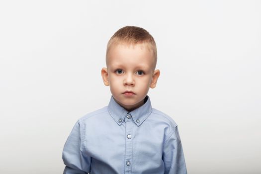 Portrait of a sad little boy in a blue shirt in front of white background in studio