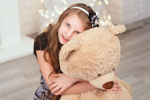 Young cute teenage girl hugs a big soft teddy bear in the interior with Christmas decorations