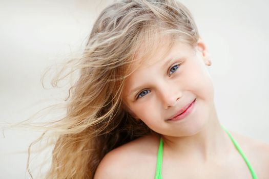 Close-up Portrait of a pretty smiling little girl with waving in the wind long hair sitting on the beach