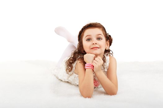 Portrait of a pretty little fun fashion girl lying on a fluffy rug on the floor against white background