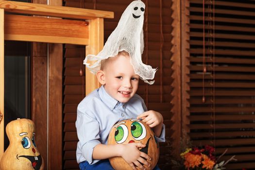 Cute Little Boy having fun in Halloween decorations. Halloween party with child holding painted pumpkin