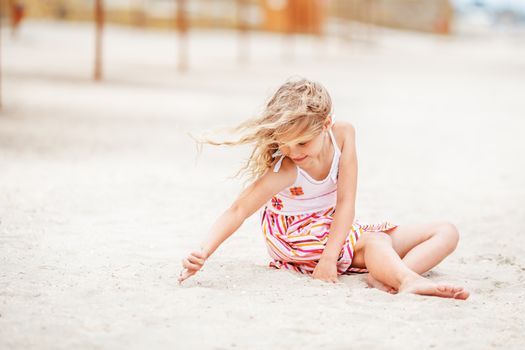 Portrait of a pretty little girl with waving in the wind long hair sitting on the beach