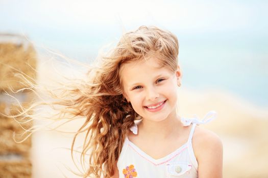 Portrait of a pretty little girl with waving in the wind long hair sitting on the beach