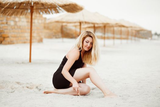 Portrait of a sexy blonde woman dreaming on a summer evening on a deserted sandy tropical beach with thatched umbrellas