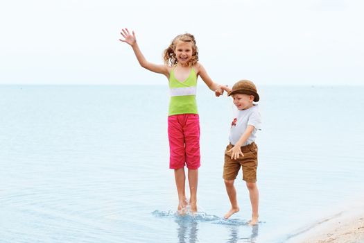 Little boy and girl jumping and having fun in water on the beach seaside. Positive emotions.