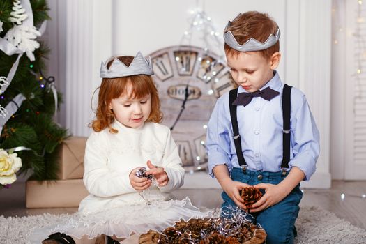 Two elegant little kids decorating Christmas tree with fir-cone. New year preparation. Happy children and family.