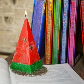 Composition of the burning red openwork handmade candles like a watermelon among colorful books. Light the candles. A burning candle. Candle lit. Candle Light