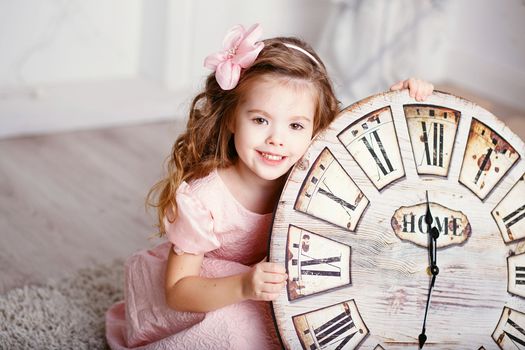 Portrait of Beautiful little girl with long curly hair in pink dress with a big clock waiting for the new year. New year preparation