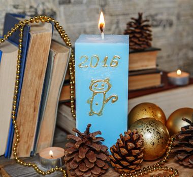 Homemade candle blue with painted golden monkey - a symbol of 2016. Decorative pine cones and candles on textured wooden surface. Handmade candles lit in vintage interior. Funny little monkey