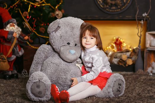 Portrait of a cute little girl hugging a soft gray teddy bear in interior with Christmas decorations