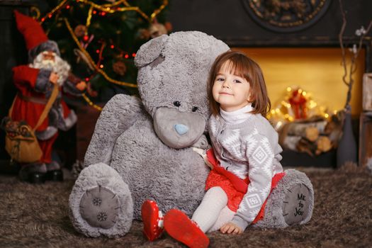 Portrait of a cute little girl hugging a soft gray teddy bear in interior with Christmas decorations