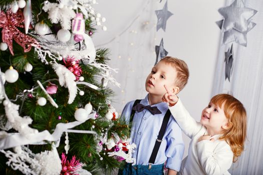 Two little kids decorating Christmas tree with toys, flowers and balls. New year preparation. Happy children and family.