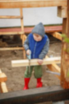 Little studious boy sawing a wooden board. Home construction. Little Helper. Little builder, blured