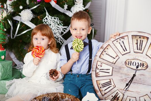 Little girl and boy eating a lollipops. Portrait of two funny little kids with a delicious candies in the hands. Christmas and New Year concept. Happy children and family In anticipation of the new year and Christmas.