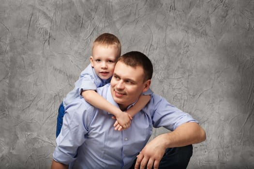 Father and little son in blue shirts in front of gray textured background