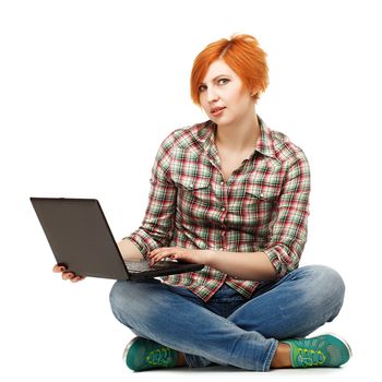 Portrait of a young pretty red-haired girl with a laptop sitting on the floor isolated on white background