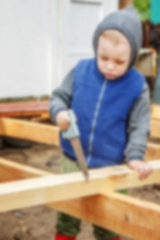 Little studious boy sawing a wooden board. Home construction. Little Helper. Little builder, blured
