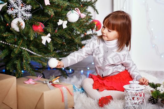 Little girl in beautiful Christmas decorations. Child decorating Christmas tree with toys and balls. New year preparation. Happy family.