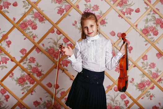 Beautiful gifted little girl playing on violin against the background of wallpaper with floral patterns and wooden lattice. Shabby chic decor