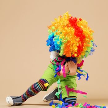 Happy clown boy with large colorful wig. Little boy in clown wig jumping and having fun. Portrait of a child throws up a multi-colored tinsel and confetti. Birthday boy.