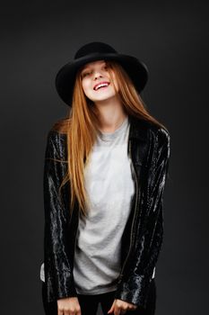 Portrait of beautiful young girl wearing black felt hat and leather jacket in front of a dark gray background