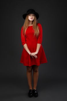 Full-length portrait of beautiful young girl in red dress and black felt hat.