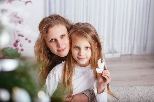 Portrait of happy smiling little girl with mother sitting near Christmas tree.