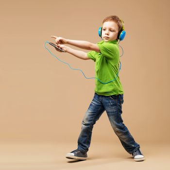 Dance! Handsome little stylish boy in headphones holding MP3 Player and dancing while standing against beige background