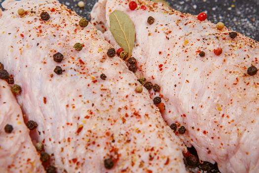 Turkey wings seasoned with pepper, salt and bay leaf. Raw turkey wings with with spices on black Slate Tray. Fresh turkey wingette with a mixture of peppers on a black stone tray