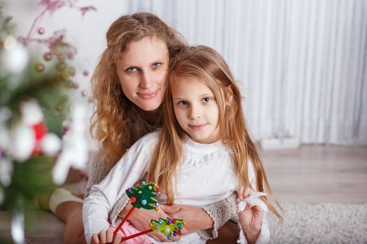 Portrait of happy smiling little girl with mother sitting near Christmas tree.