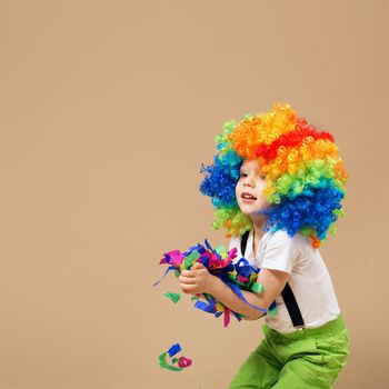 Happy clown boy with large colorful wig. Little boy in clown wig jumping and having fun. Portrait of a child throws up a multi-colored tinsel and confetti. Birthday boy.