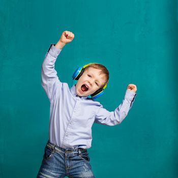 Dance! Handsome little stylish boy in headphones dancing while standing against green blue wall