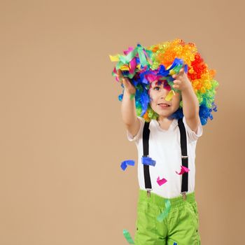 Happy clown boy with large colorful wig. Little boy in clown wig jumping and having fun. Portrait of a child throws up a multi-colored tinsel and confetti. Birthday boy.