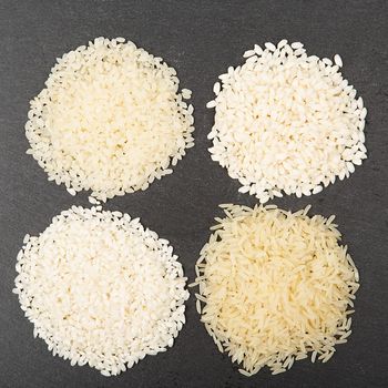 Rice background, uncooked raw cereals, macro closeup. Various color and shape varieties of rice on black slate tray