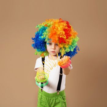 Happy clown boy with large colorful wig. Little boy in clown wig playing with a spring. Birthday boy. Positive emotions.