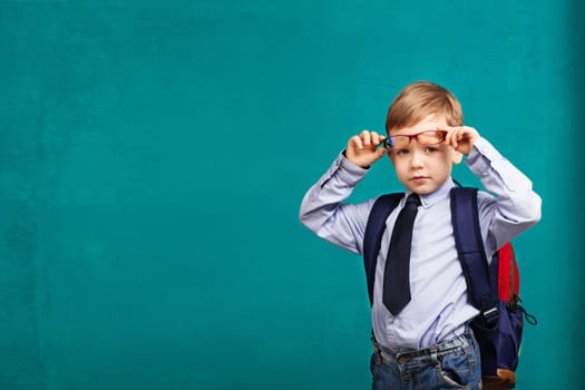 little Boy in eyeglasses with big backpack. School, kid, rucksack. Cheerful smiling little kid against chalkboard. Looking at camera. School concept. Back to School