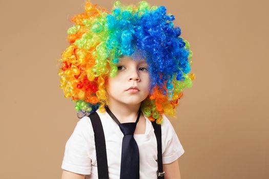 Sad clown. Little boy in clown wig smilling and having fun. Thoughtful clown boy with large colorful wig. Birthday boy. Little clown boy with colorful hair. Positive emotions.