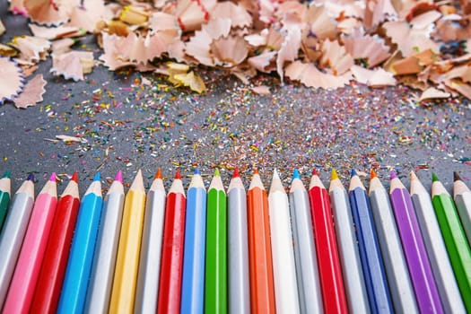 close up shot of colored pencil crayons and pencil crayons shavings on dark background. Sharpened colored pencils on gray background.