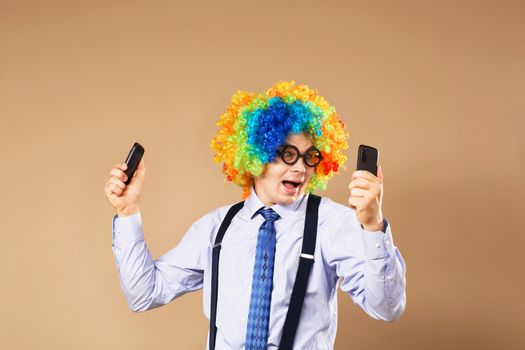 Businessman respond to numerous phone calls. Businessman holding two mobile phones. Close-up Portrait of business man in clown wig. Business concept. Multitasking