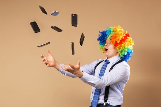 Businessman catching mobile phones falling from above. Close-up Portrait of business man in clown wig. Business concept