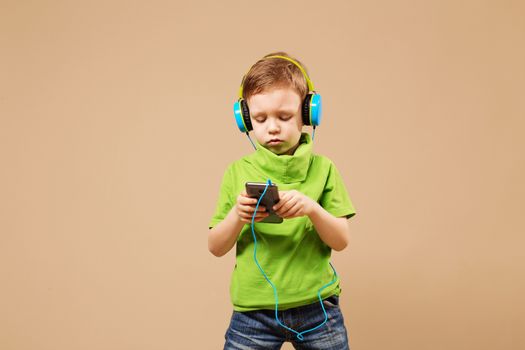 boy ware headphone and playing the cell phone on beige background. boy in the headphones enjoy music. young boy is listening to music