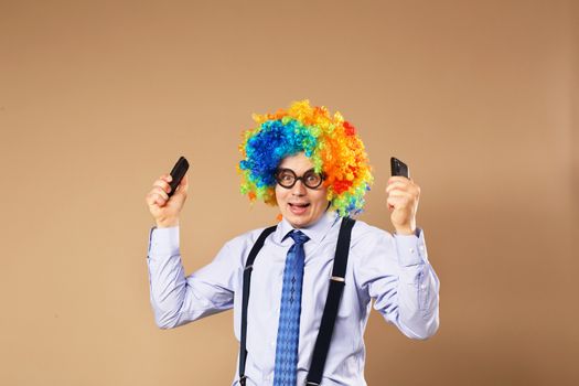 Businessman respond to numerous phone calls. Businessman holding two mobile phones. Close-up Portrait of business man in clown wig. Business concept. Multitasking