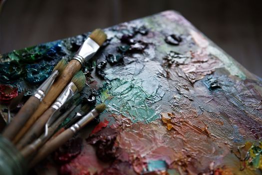 artists brushes and oil paints on wooden palette. macro artist's palette, texture mixed oil paints in different colors and saturation. palette with paintbrush and palette-knife