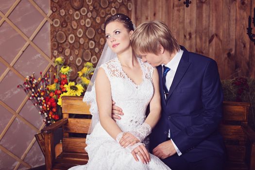 Bride and groom sitting on a bench in studio with vintage interior. Photo of happy newlyweds