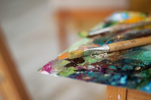 artists brushes and oil paints on wooden palette. macro artist's palette, texture mixed oil paints in different colors and saturation. palette with paintbrush and palette-knife