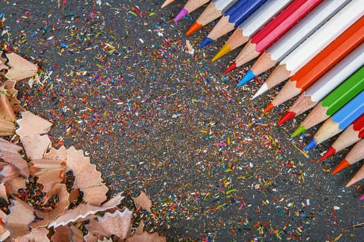 close up shot of colored pencil crayons and pencil crayons shavings on dark background. Sharpened colored pencils