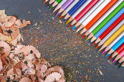close up shot of colored pencil crayons and pencil crayons shavings on dark background. Sharpened colored pencils on gray background.